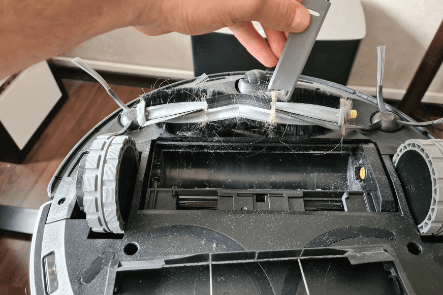 Haare werden aus der Hauptbürste eines Saugroboters mit Hilfe eines speziellen Reinigungswerkzeugs entfernt.